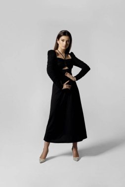 Siyah elbiseli güzel bir kadın beyaz arka planda poz veriyor..