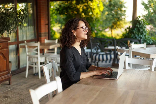 坐在阳台上的一位在笔记本电脑上工作的快乐的年轻女性的肖像 — 图库照片