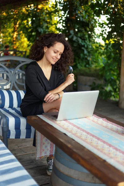 一个快乐的年轻女人坐在阳台上 在笔记本电脑上工作 纵向观点 — 图库照片