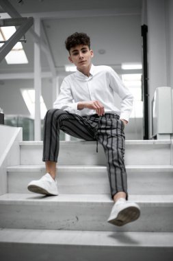 Çekici, neşeli, yakışıklı genç erkek model merdivenlerde poz veriyor ve kameraya bakıyor..
