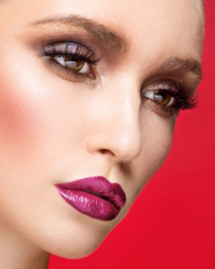 Mükemmel makyajlı, kırmızı arka planda izole edilmiş genç bir kadın modelin yakın plan görüntüsü..