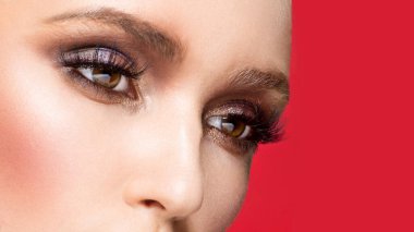 Kırmızı arka planda izole edilmiş, mükemmel makyajlı bir kadının yakın plan görüntüsü. Makyajlı bir kadın gözünün kesilmiş görüntüsü..