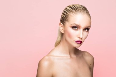 Güzel makyajlı ve saçı arkadan çekilmiş genç bir kadının ön portresi. Kameraya bakıyor, izole edilmiş pembe bir arka plan..