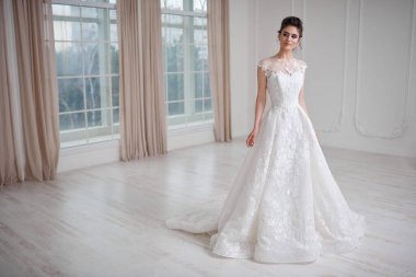 Güzel elbiseli, güzel esmer bir gelinin beyaz stüdyoda pencereli bir şekilde poz verişi..