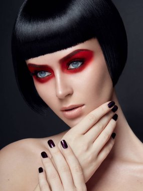Kırmızı dudaklı ve siyah kısa saçlı güzel esmer kız. Siyah saçlı güzel bir genç kadın. Yüzünde parlak makyaj olan bir modelin yakın plan portresi. Güzel bir bayanın moda portresi..