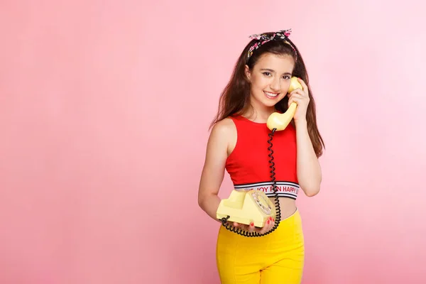 Leende söt flicka, talar på gammaldags telefon på en rosa bakgrund, plats för text. Horisontell vy. — Stockfoto