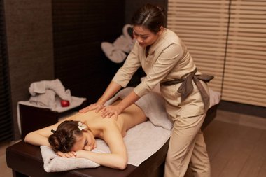 Masöz, genç bir kadının sırtına masaj yapıyor. Yatay görünüm.