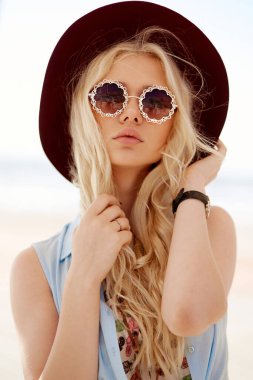 Closeup front image of a blonde with round eyeglasses, big lips,wavy hair and burgundy hat.