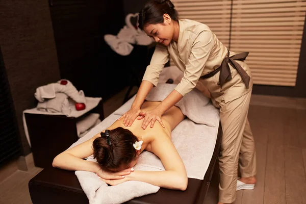 Back image of a the masseuse massages the back of a young woman.