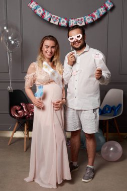 Cinsiyet belirleme partisinde, balon ve konfeti eşliğinde yazıtları tutan mutlu çift..