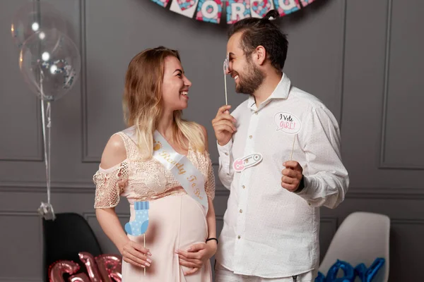 Mutlu bir çiftin ön portresi. Ellerinde yazıtlar, yüzlerinde maske olan bir erkek ya da kız var. Cinsiyet teşhisi sırasında birbirlerine bakıyorlar..