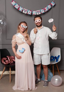 Cinsiyet ayrımcılığı sırasında elinde yazı tutan gülümseyen bir çiftin tam boy fotoğrafı sahne donanımları ve balonlar üzerinde partiyi gözler önüne seriyor..