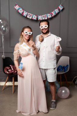 Cinsiyet ayrımcılığı sırasında elinde yazı tutan gülümseyen bir çiftin tam boy görüntüsü sahne donanımları ve balonlar üzerindeki partiyi gözler önüne seriyor..