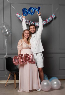Mutlu bir çiftin cinsiyet belirleme partisinde, balonlar üzerinde yazılı bir erkek ya da kız tutarken tam boy görüntüsü..