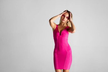 Front image of a sexy blonde female model in pink slim dress isolated on grey background. Copy space.