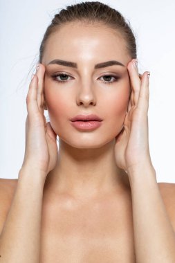 Doğal makyajlı genç bir kadının yakın plan ön portresi, yan tarafa bakıyor, yüzüne yakın el ele tutuşuyor.