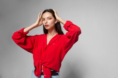 Genç, güzel, esmer, gündelik kırmızı tişörtlü, uzun saçlı, izole, gri arka planlı bir kadın.