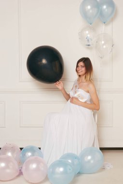 Beautiful pregnat sit on chair holding a black balloon.