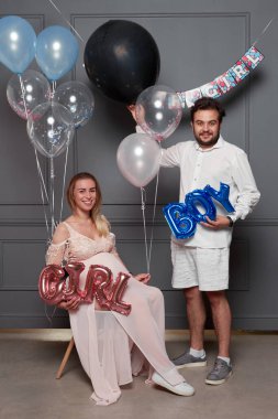 Cinsiyet ayrımcılığı sırasında sürpriz balon şişiren heyecanlı genç bir çiftin tam boy görüntüsü içeride parti olduğunu gösteriyor.