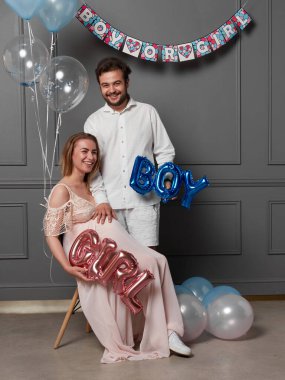 Cinsiyet ayrımcılığı sırasında balon tutan genç ve heyecanlı bir kadın ve erkeğin tam boy görüntüsü stüdyoda poz verdiklerini gösteriyor.