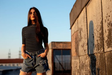 Güzellik insanları. Çatıda şehvetle poz veren hayalperest genç kadının portresi, gün batımında gözleri kapalı. Yatay görünüm.