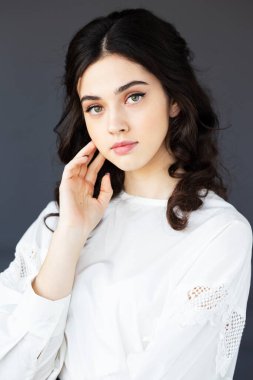 Gülümseyen genç bir kadının ön portresi beyaz gömlek giyer, bir stüdyoda kameraya bakar, izole edilmiş gri arka plan..