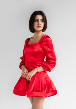 Stüdyoda poz veren, saç stili ve makyajlı, gri arka planda beyaz elbiseli genç bir kadın..