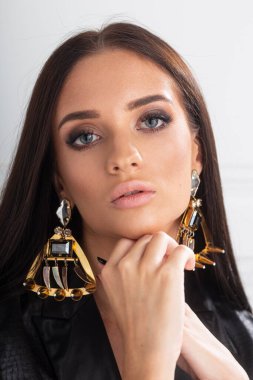 Deri ceketli, beyaz arka planda kameraya bakan seksi esmer kadın..