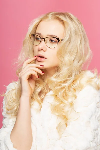 Closeup frontal portrait of a blonde young woman with makeup wearing eyeglasses, isolated pink background.