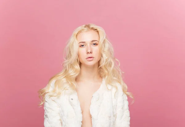 Closeup frontal portrait of a blonde young woman with makeup wearing eyeglasses, isolated pink background.