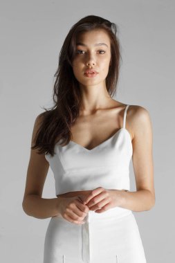 Makyaj ve saç stili olan, beyaz giyinmiş esmer bir kadının ön portresi, izole beyaz arka planda, sandalyeye oturuyor..