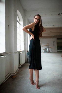 Siyah elbiseli çekici genç bir kadının tam boy görüntüsü. Yan tarafa bakıyor, stüdyoda poz veriyor..