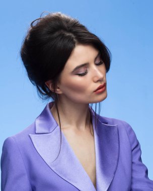 Side view of a sexy brunette in a stylish purple suit in attractive, looking at camera, isolated blue background.