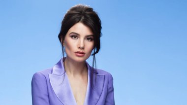 Front image of a sexy brunette in a stylish purple suit in attractive, looking at camera, isolated blue background. Space for text.