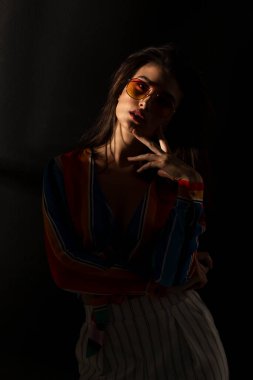 Yakından bakınca, renkli kıyafetler ve güneş gözlüğü takan, gözleri kapalı, esmer genç bir kadın görünüyor. Dikey görünüm.