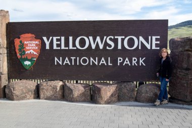 Yellowstone Ulusal Parkı 'nın kuzey girişindeki tabelasının yanında duran kadın turist.