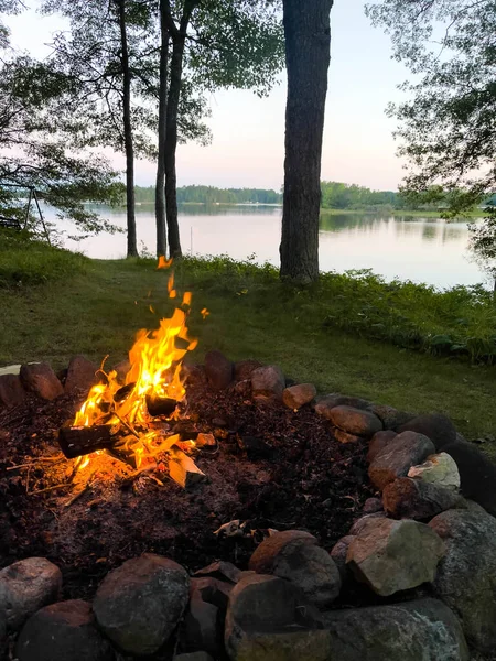Campfire next to a calm lake in the summer, vertical