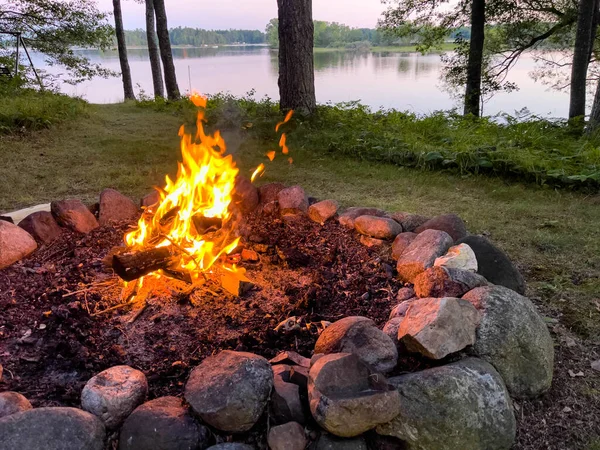 Campfire next to a calm lake in the summer, horizontal