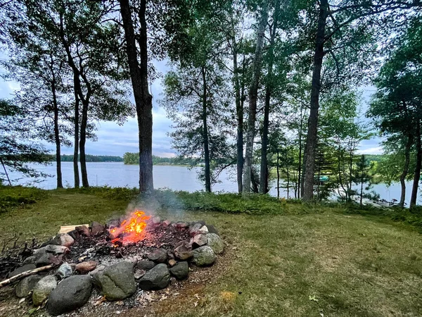 Campfire next to a calm lake in the summer, horizontal