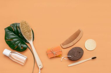 Sıfır atık taraklı banyo aksesuarları, ahşap diş fırçası, katı sabun, kozmetik kavanozu, ahşap tarak, bej arka planda bir yaprak dolusu canavar olan sünger..