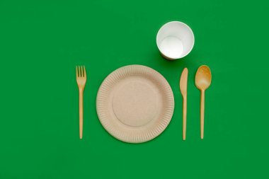 Yeşil arka planda geri dönüşümlü çatal, kaşık, bıçak, tabak ve bardak. Mutfak aletleri. Üst Manzara. Minimalist stil. Boşluğu kopyala.