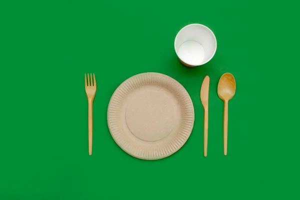 Yeşil arka planda geri dönüşümlü çatal, kaşık, bıçak, tabak ve bardak. Mutfak aletleri. Üst Manzara. Minimalist stil. Boşluğu kopyala.