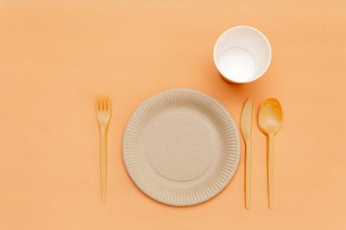 Bej arka planda geri dönüşümlü çatal, kaşık, bıçak, tabak ve bardak. Mutfak aletleri. Üst Manzara. Minimalist stil. Boşluğu kopyala.