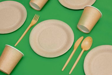 Yeşil arka planda geri dönüşümlü çatal, kaşık, bıçak, tabak ve bardak. Mutfak gereçleri masada servis edilir. Üst Manzara. Minimalist stil. Boşluğu kopyala.