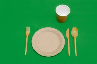 Yeşil arka planda geri dönüşümlü çatal, kaşık, bıçak, tabak ve bardak. Mutfak aletleri. Üst Manzara. Minimalist stil. Boşluğu kopyala.