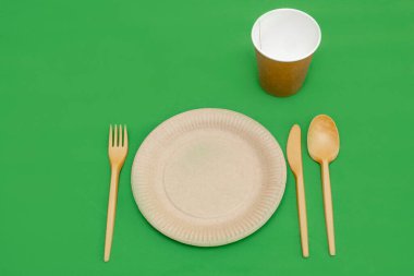 Yeşil arka planda geri dönüşümlü çatal, kaşık, bıçak, tabak ve bardak. Mutfak aletleri. Üst Manzara. Minimalist stil. Boşluğu kopyala.