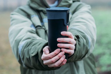 Kadınların elleri, sonbaharın sonlarında sıcak bir içecekle kendilerini siyah şalter düğmesinde ısıtıyorlar. Yeniden kullanılabilir bardakların çevre dostu kullanımı