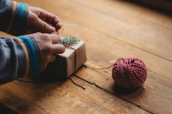 圣诞礼物包装 男人们的手穿着蓝色毛衣 在木制桌子上的小礼品盒上绑着一个蝴蝶结 有选择的重点 — 图库照片
