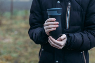 Sonbaharın sonlarında, erkeklerin elleri sıcak bir içecekle kendilerini siyah bir düğmede ısıtıyorlar. Yeniden kullanılabilir bardakların, kupaların çevre dostu kullanımı. Plastiğin reddi.