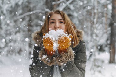 Mutlu bir genç kız, sıcak örülmüş hardal renkli eldivenlere uzanan beyaz kara üfledi. Ön planda bulanık kar taneleri. Noel tatili, kış zamanı. Yüzü olmayan.